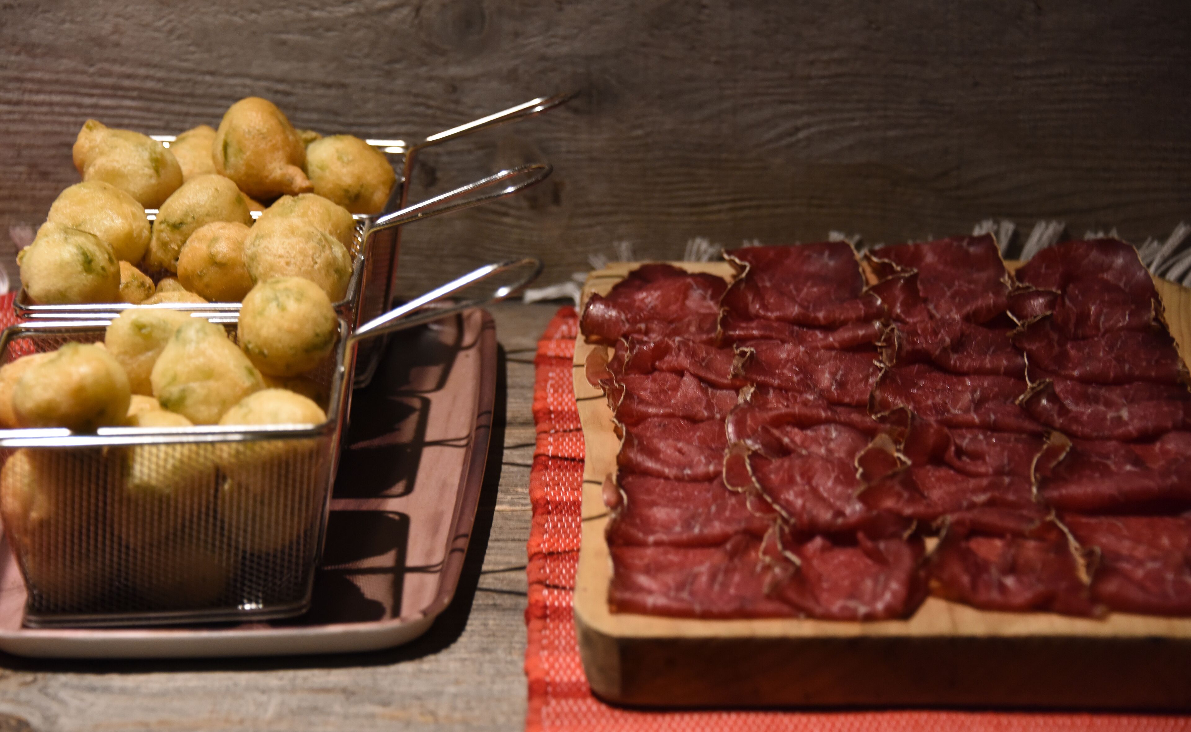 A tray of fried dough balls and a wooden board with sliced meat.