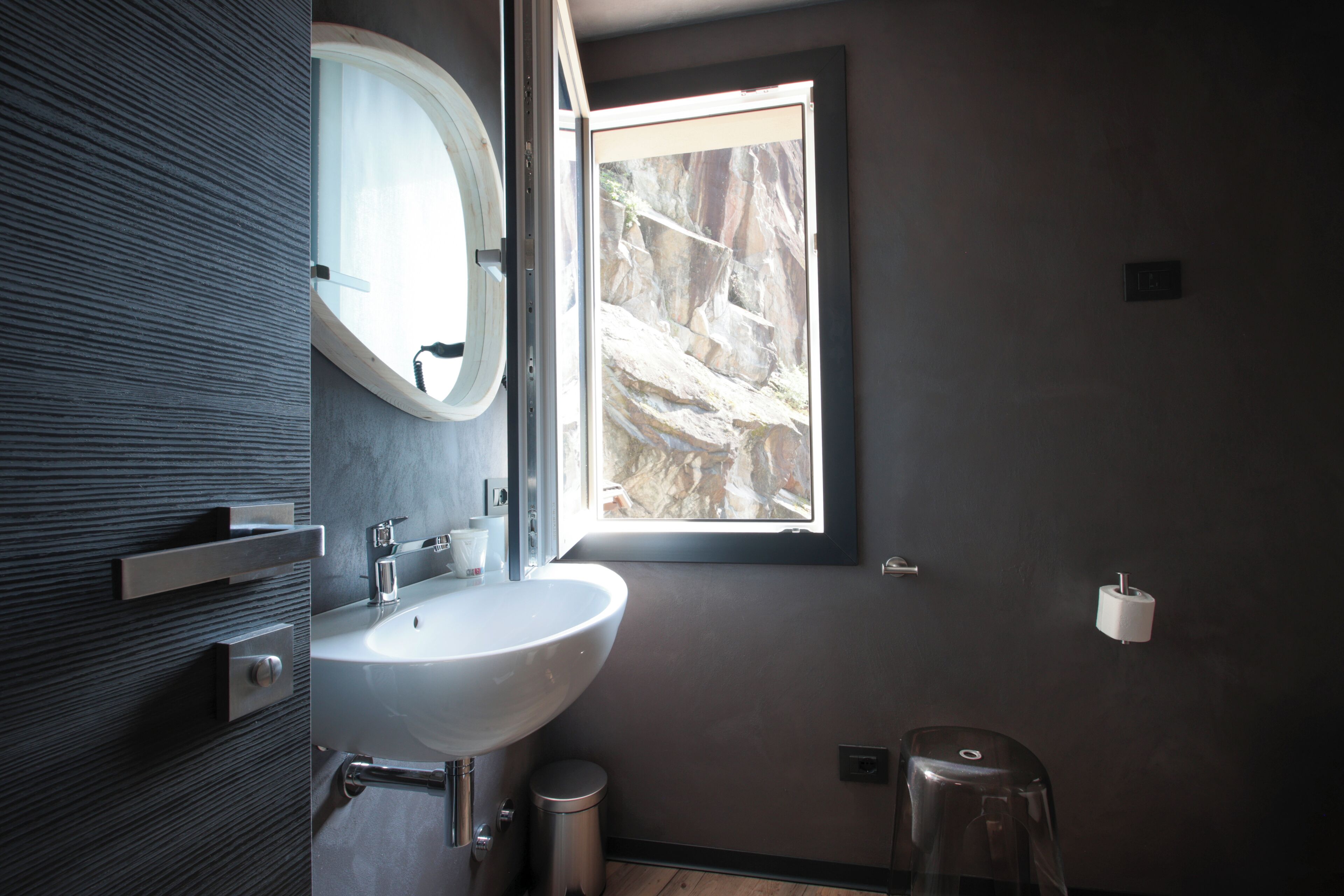 Un baño moderno con un lavamanos grande, un espejo y una ventana con vistas a terreno rocoso.
