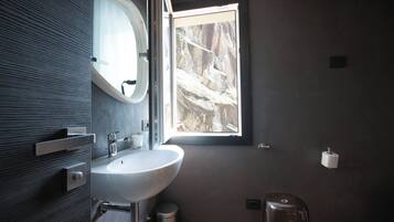 Un baño moderno con un lavamanos grande, un espejo y una ventana con vistas a terreno rocoso.