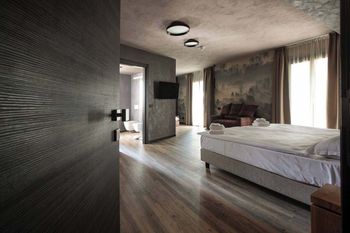 A modern hotel room with a large bed, a flat-screen TV, and a view of the outdoors.