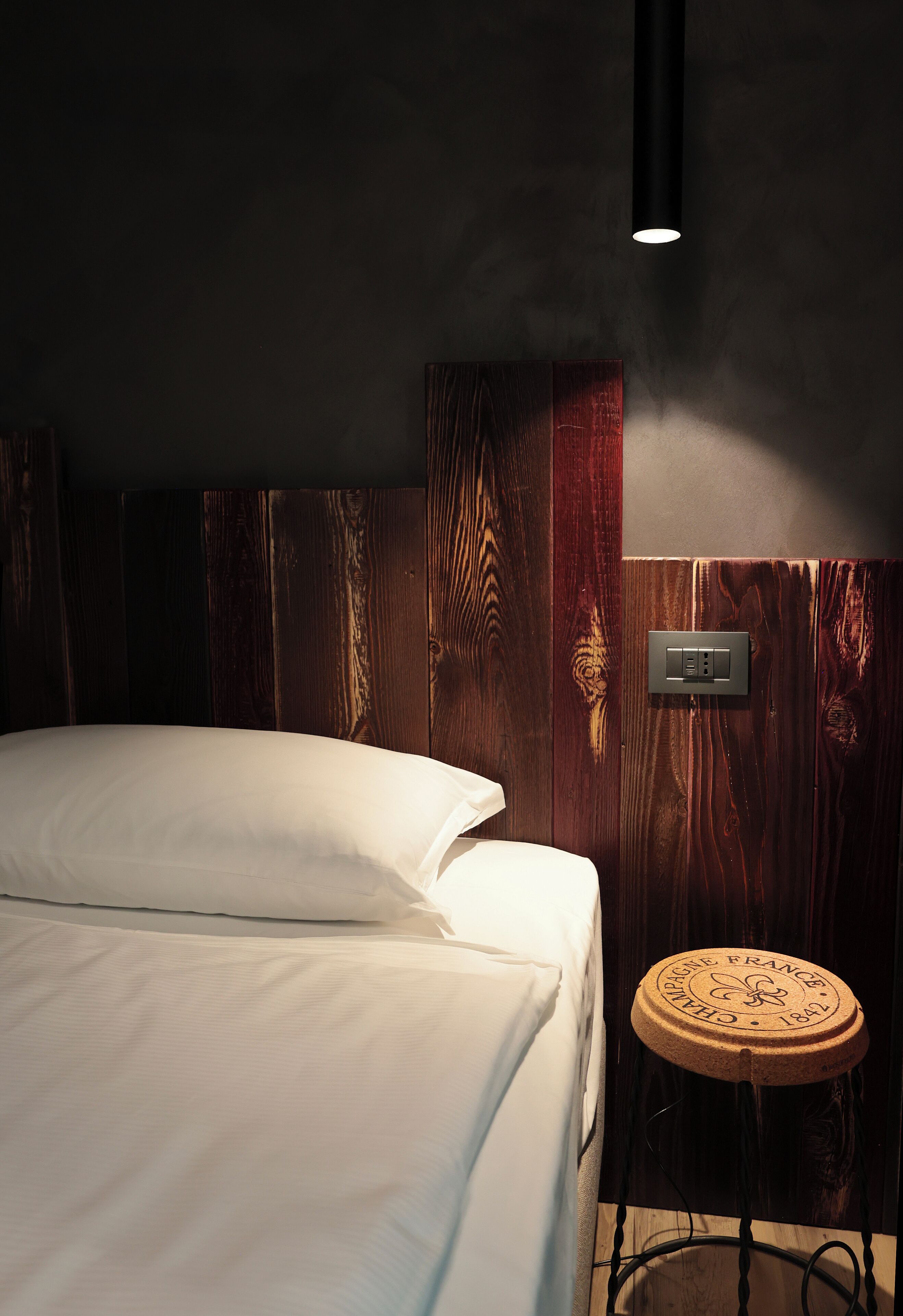 Ein Schlafzimmer mit einem Bett, einem runden Holzschemel und einer Wandleuchte.