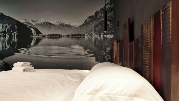 Habitación de hotel con una cama, vista a un lago, montañas y una pared de madera.