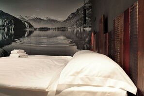 A hotel room with a bed, a view of a lake, mountains, and a wooden wall. - Crimea Wine Hotel (Chiavenna)