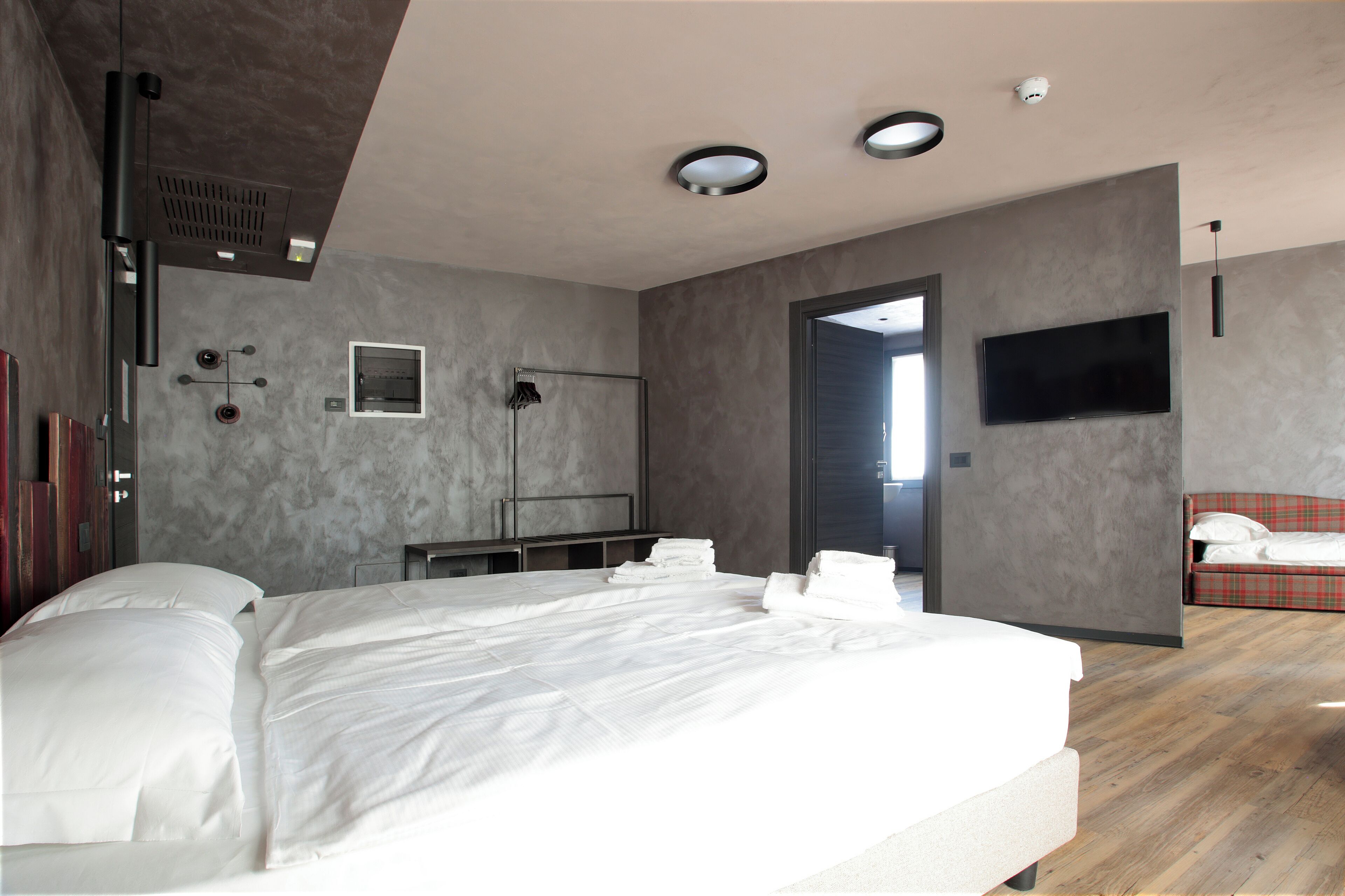 Un dormitorio moderno con una cama grande, un televisor de pantalla plana en la pared y un sofá rojo a cuadros en la esquina.