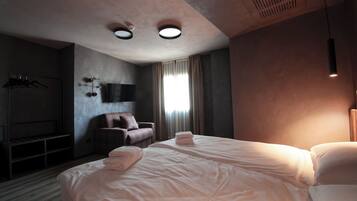 Quarto de hotel com uma cama grande, uma cadeira, uma televisão e um guarda-roupa.