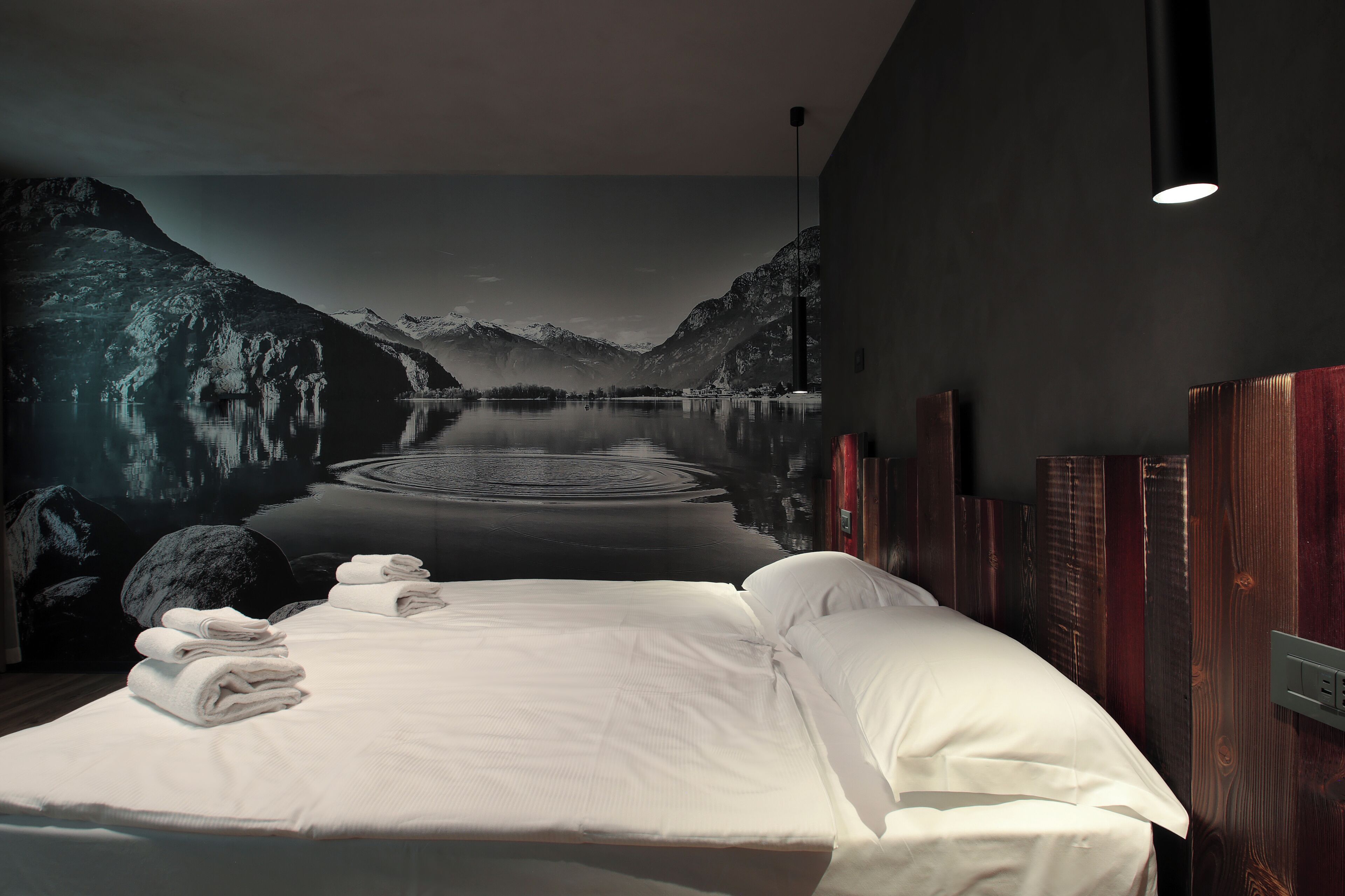 A hotel room with a large bed, neatly folded towels, a wooden headboard, and a mural of a mountain lake.