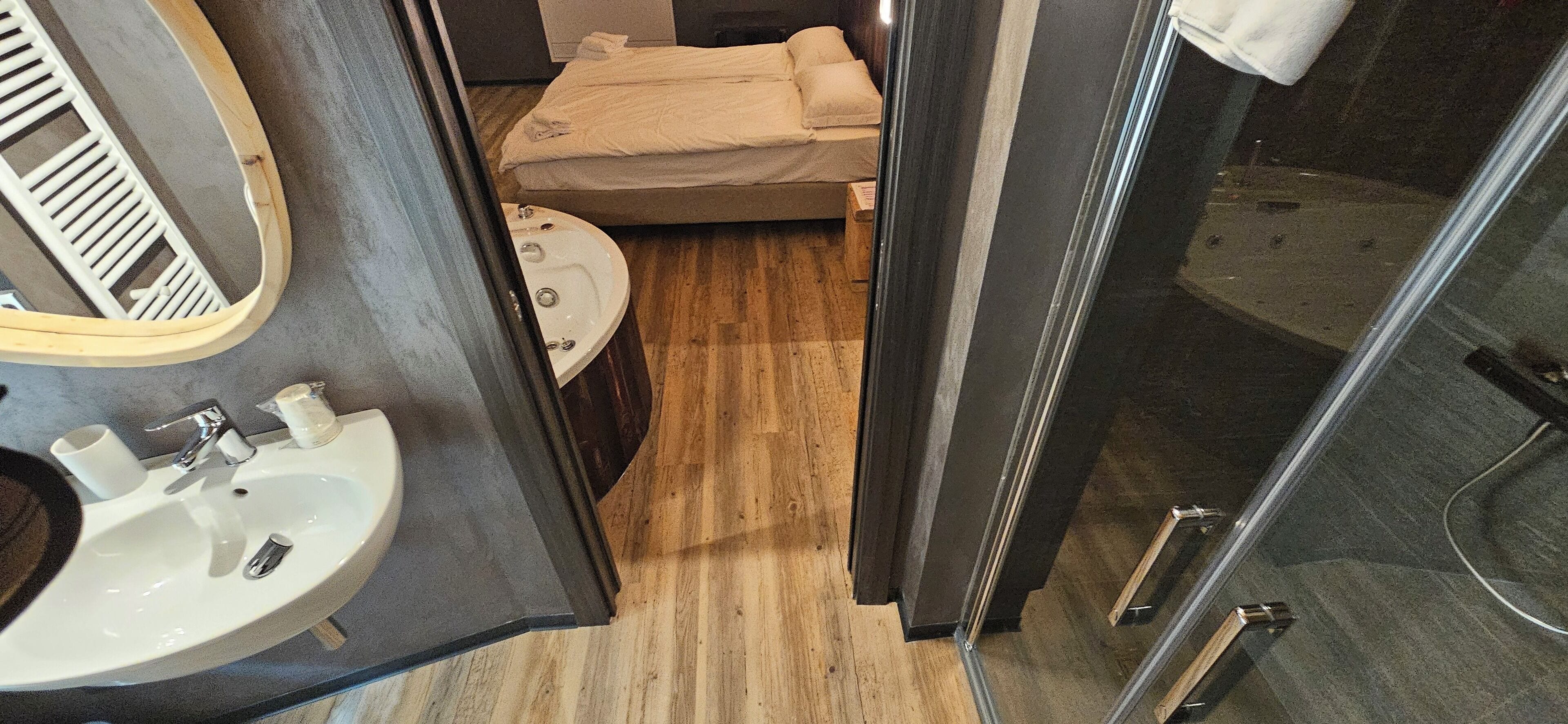 Casa de banho compacta com lavatório, espelho e cama sobre um chão de madeira.
