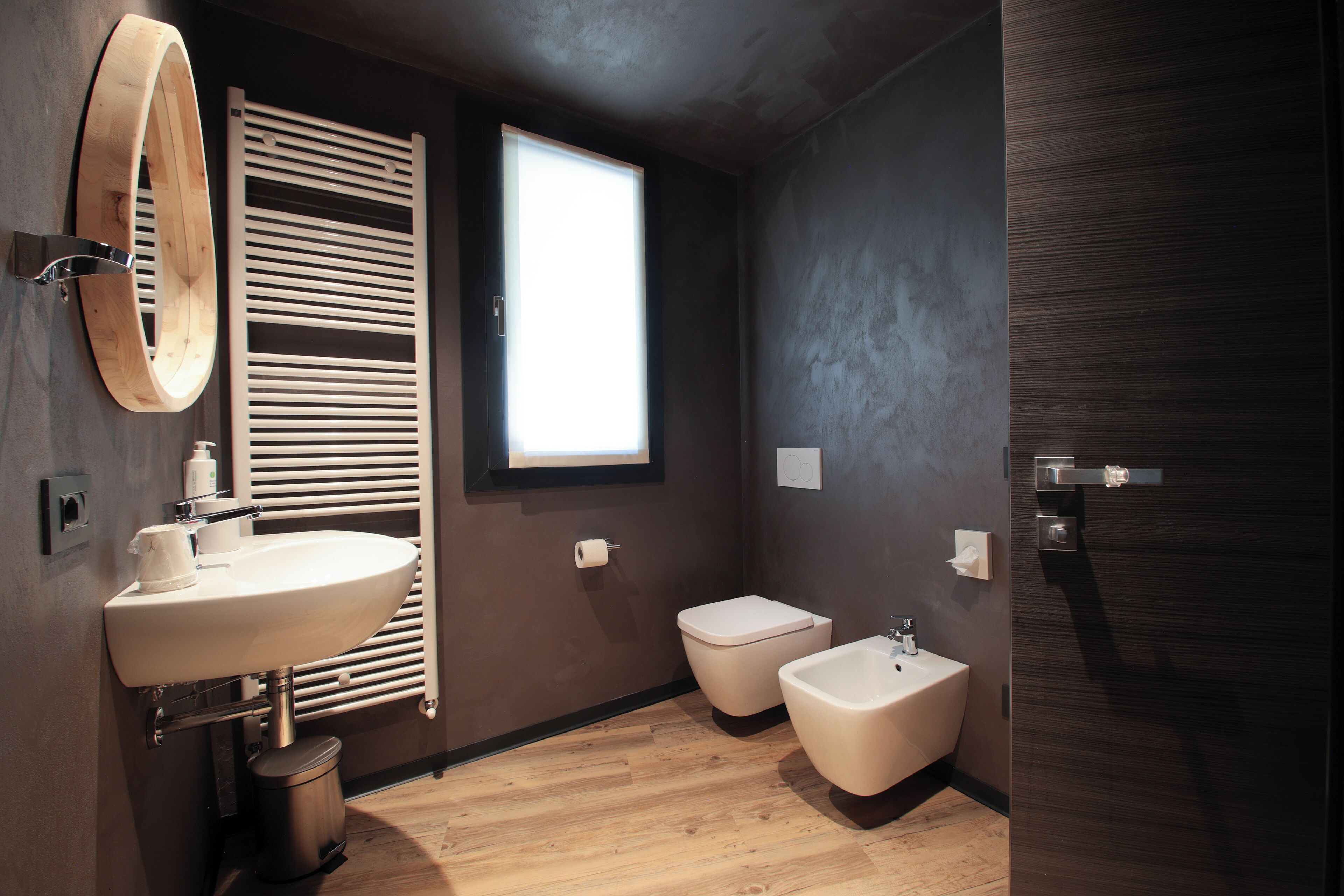 Un baño moderno con tocador de madera, dos inodoros, un bidé y un ventanal que proporciona luz natural.