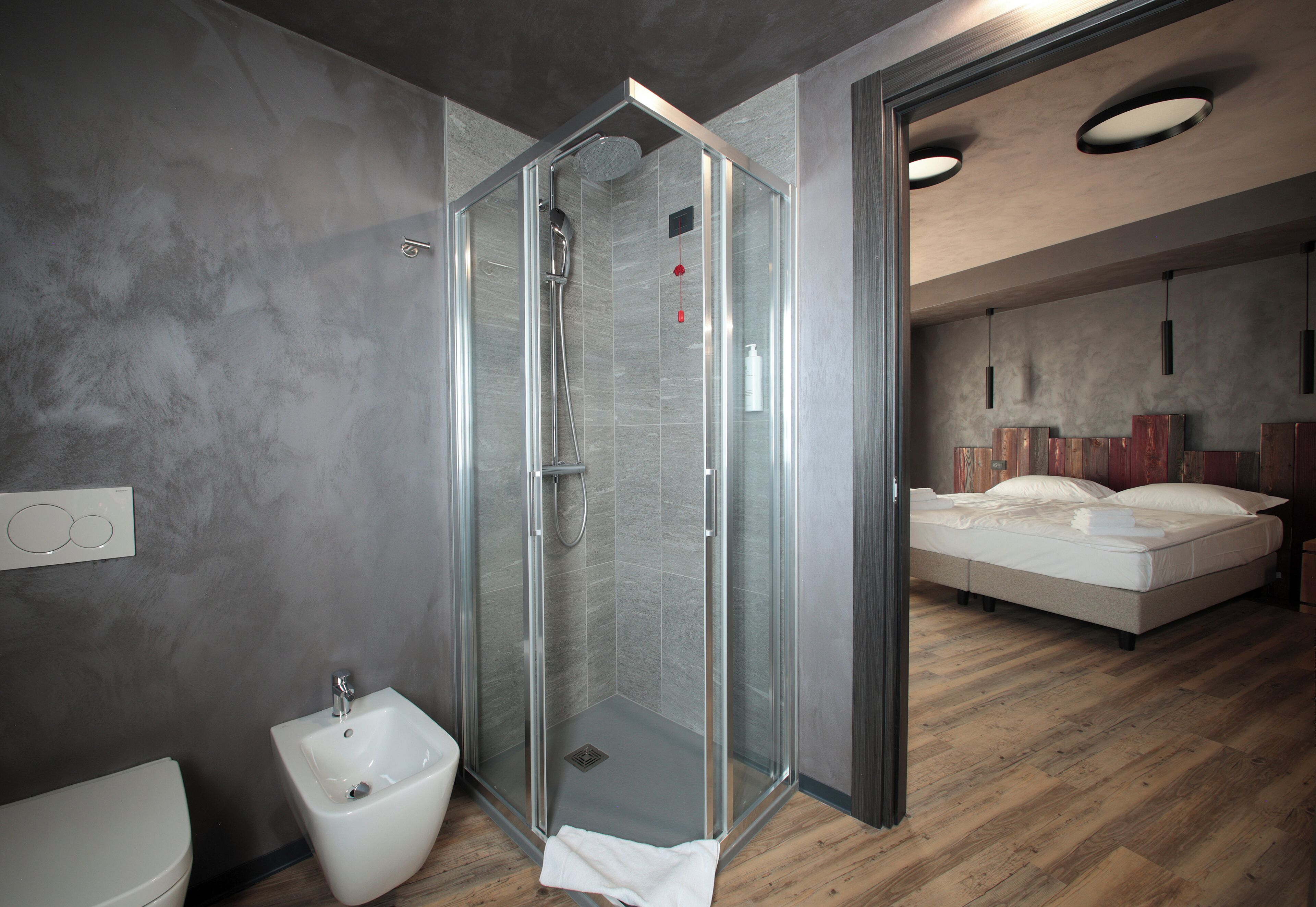 A modern bathroom with a glass shower enclosure, a bidet, and a wooden floor.