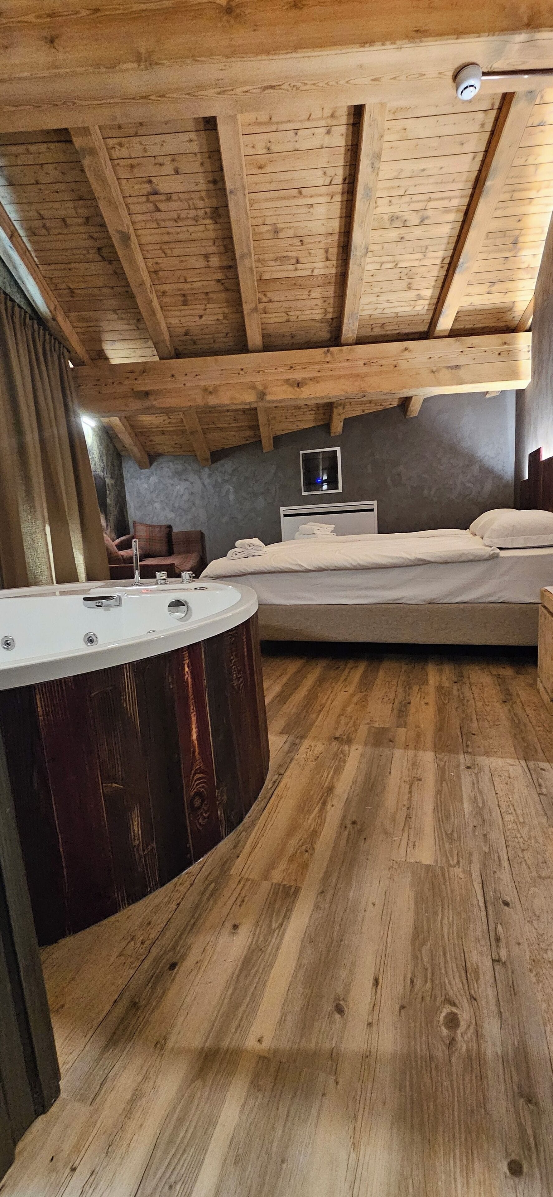 A bedroom with a wooden ceiling, a bed, a nightstand, and a bathtub.