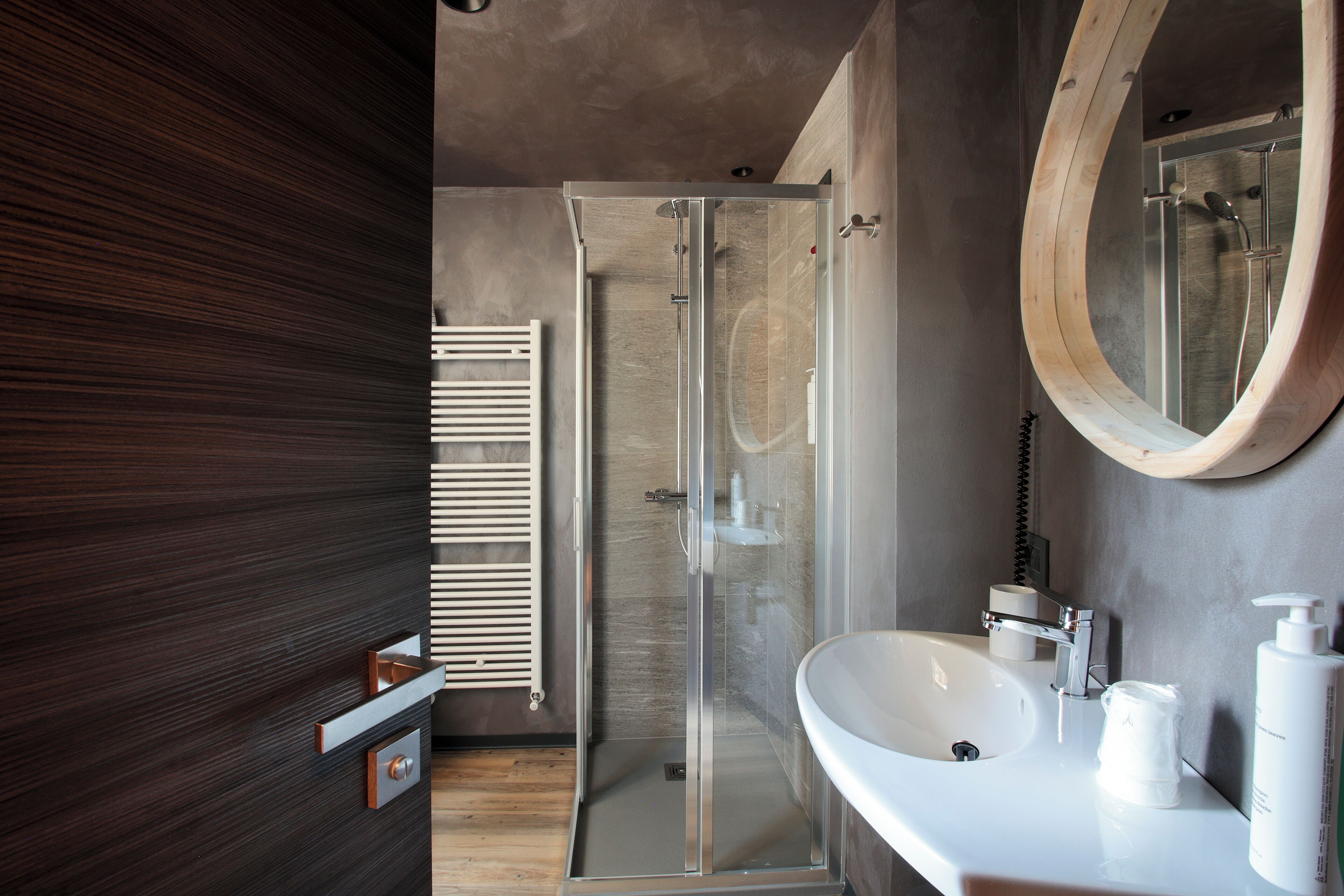 A modern bathroom with a glass shower enclosure, a white sink, and a wooden-framed mirror.