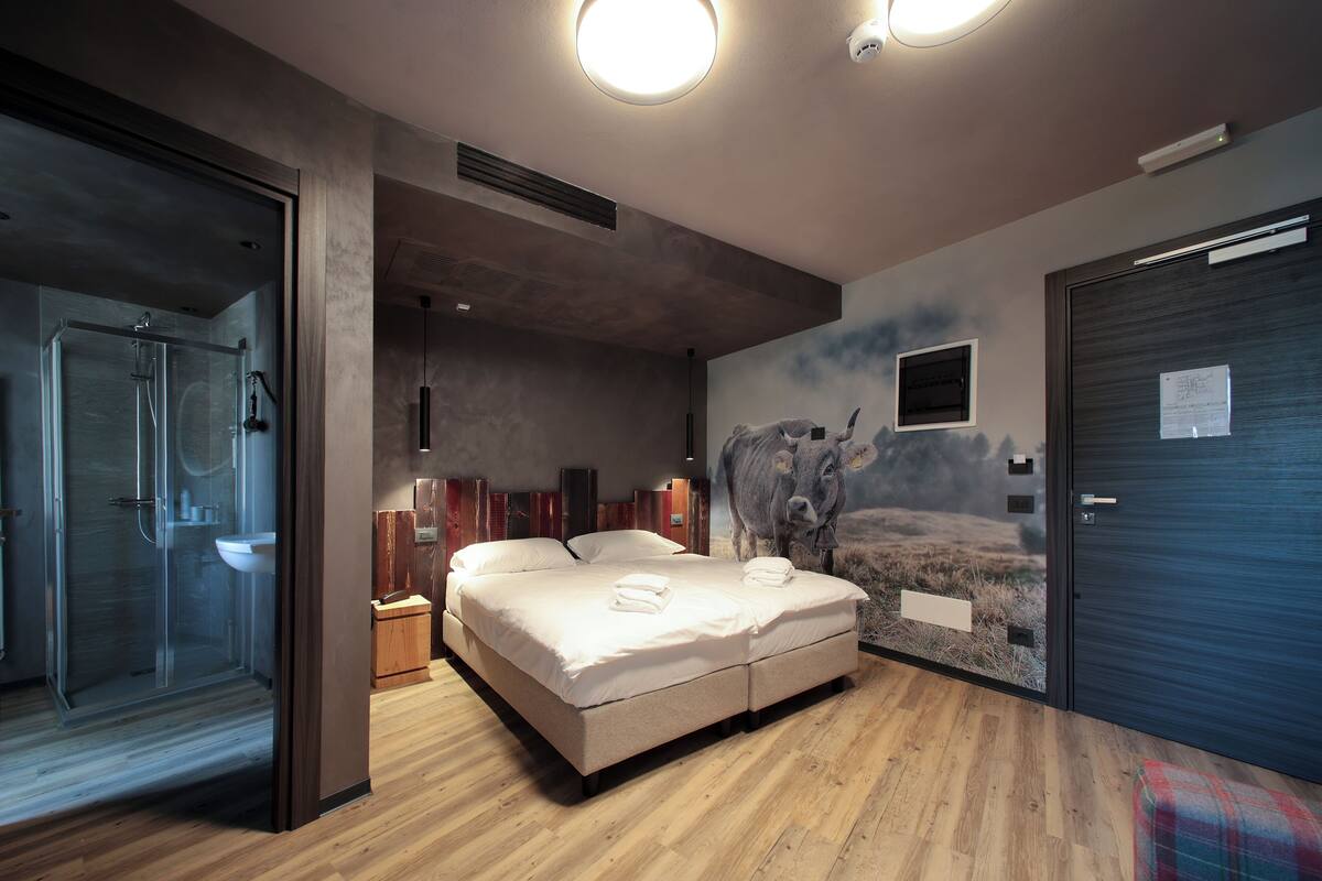 A modern bedroom with a large bed, a glass shower enclosure, and a cow mural on the wall.