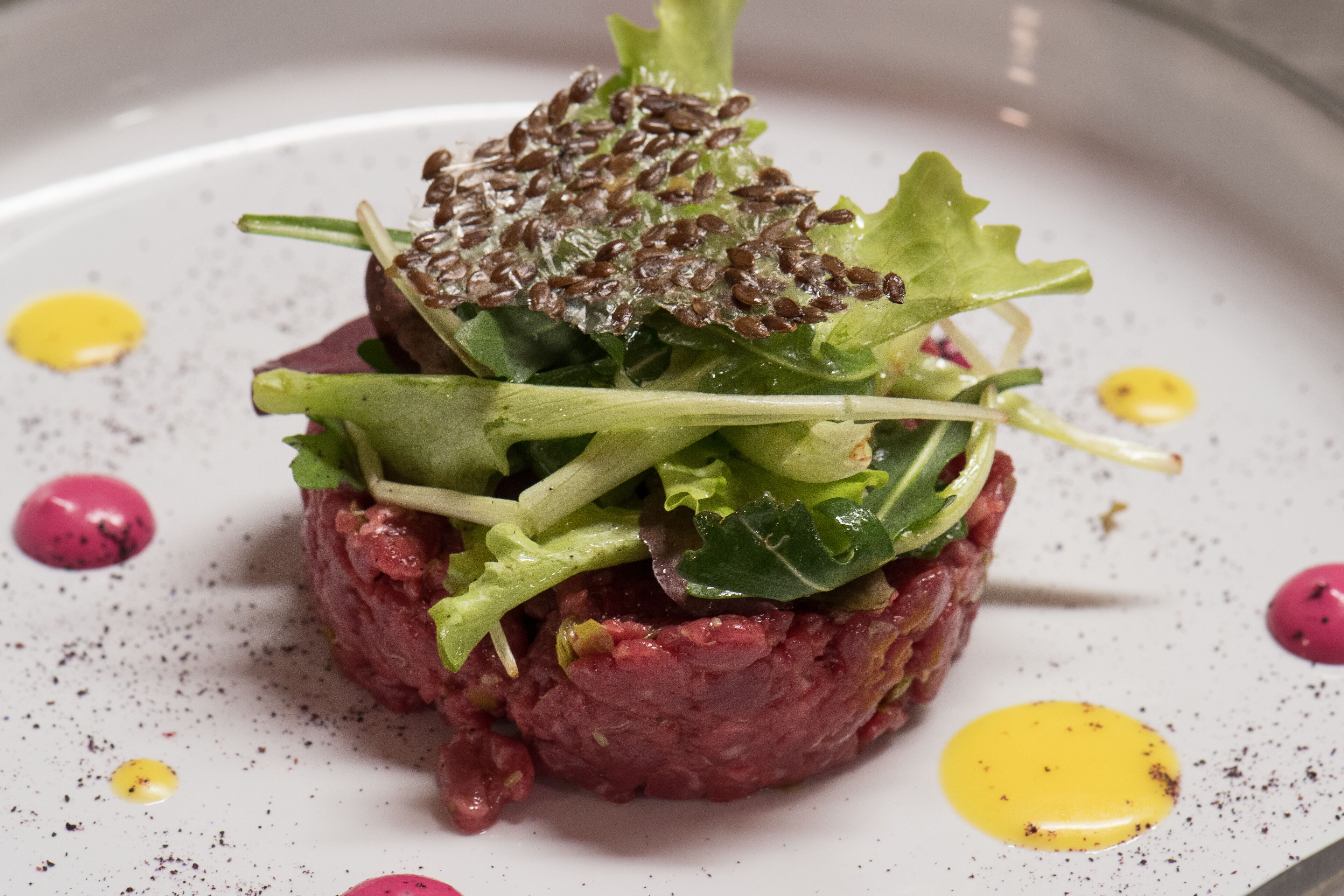 Un plato con carne, vegetales y semillas, decorado con puntos amarillos y rosados.