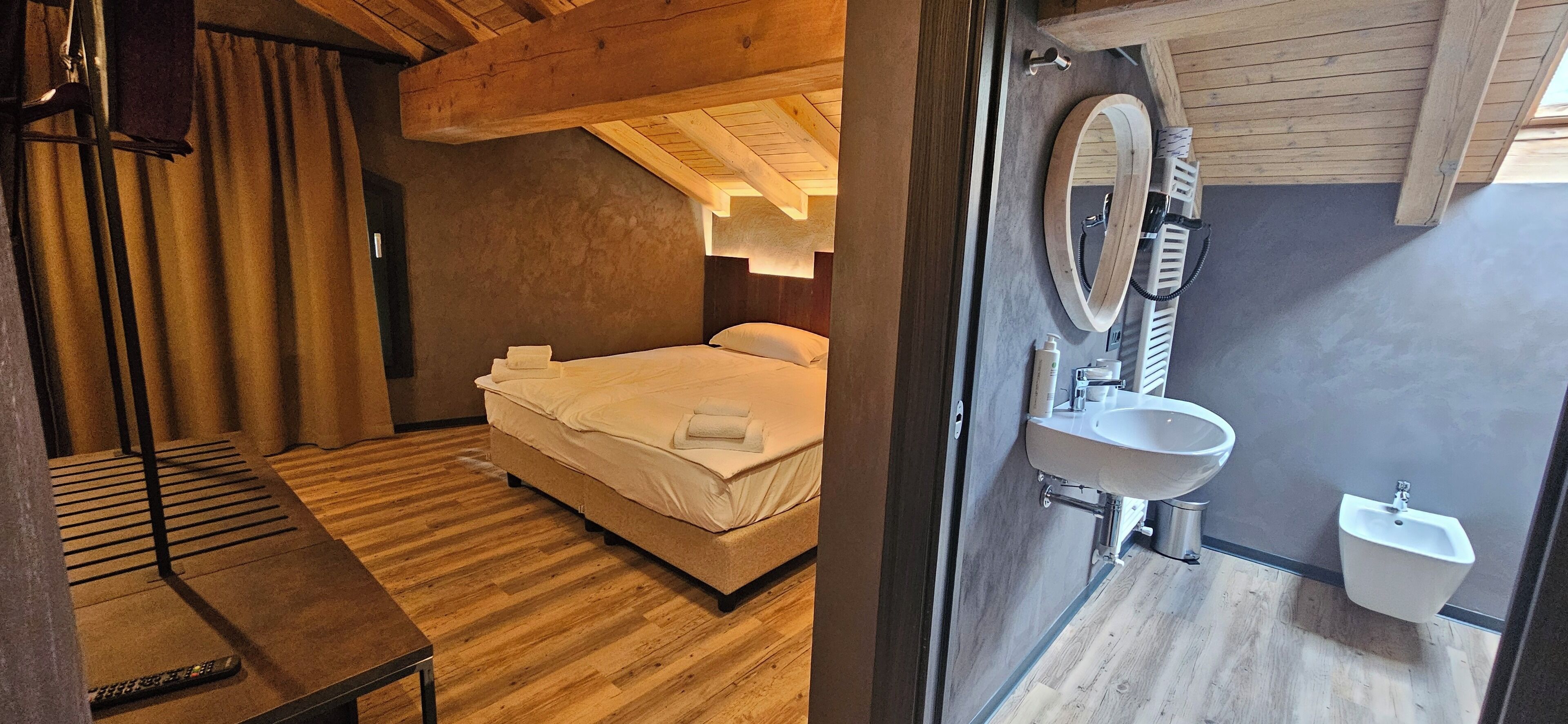 A bedroom with a bed, bedside table, and a wooden ceiling. The bathroom includes a sink, mirror, and bidet.