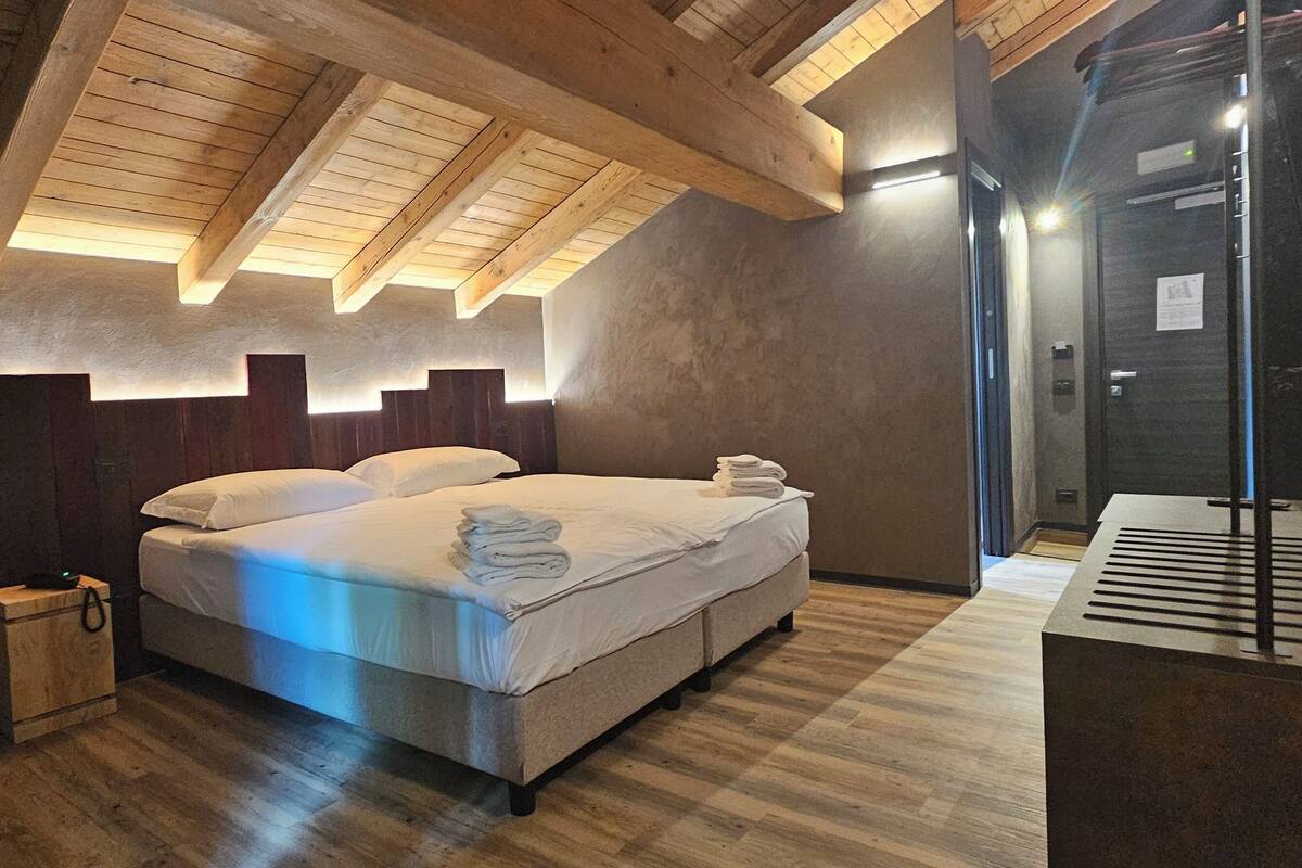 A modern bedroom with a wooden ceiling, a bed with white linens, and a dark door.