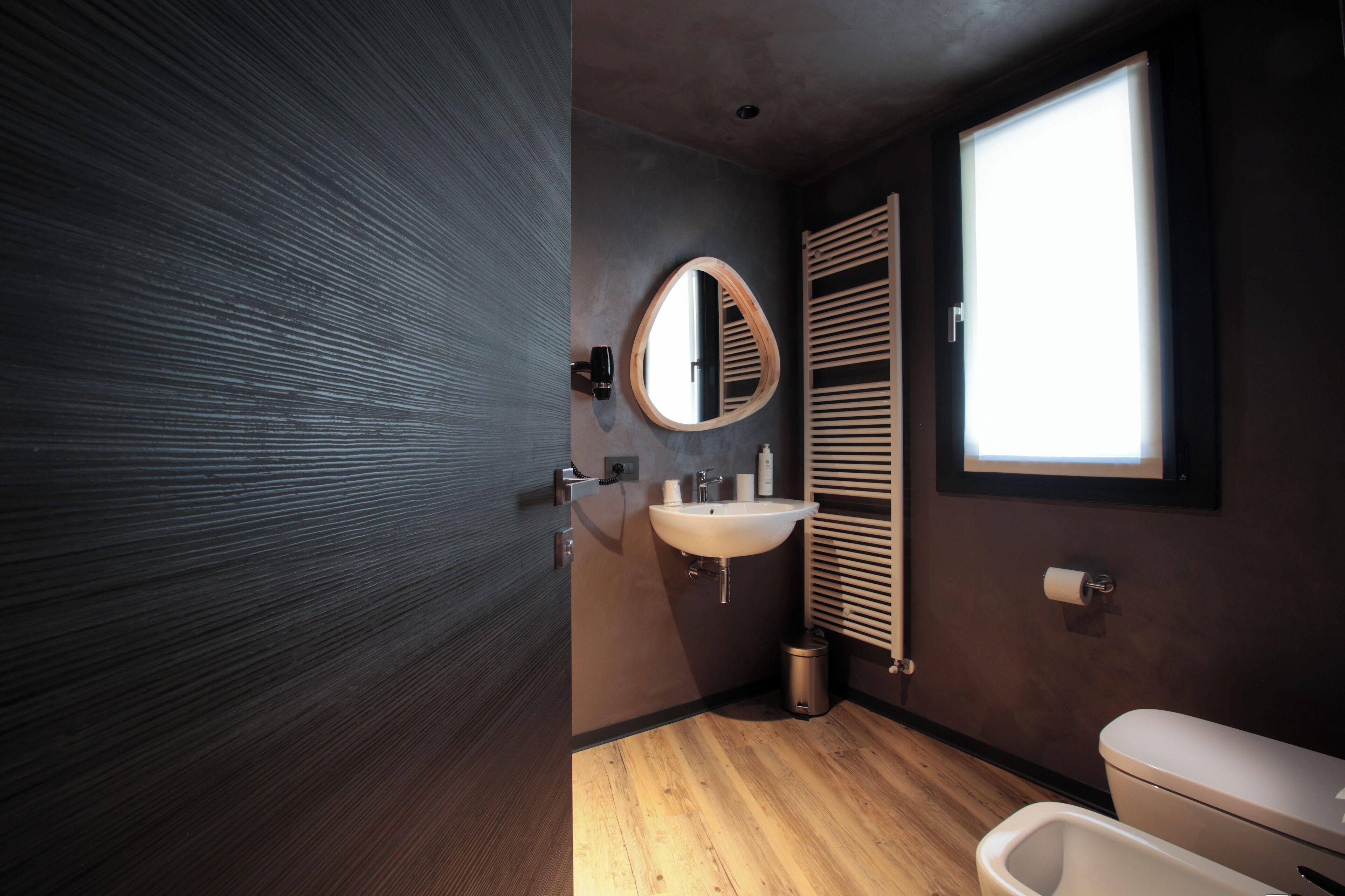Un bagno moderno con pavimento in legno, uno specchio rotondo, un lavabo e un water.