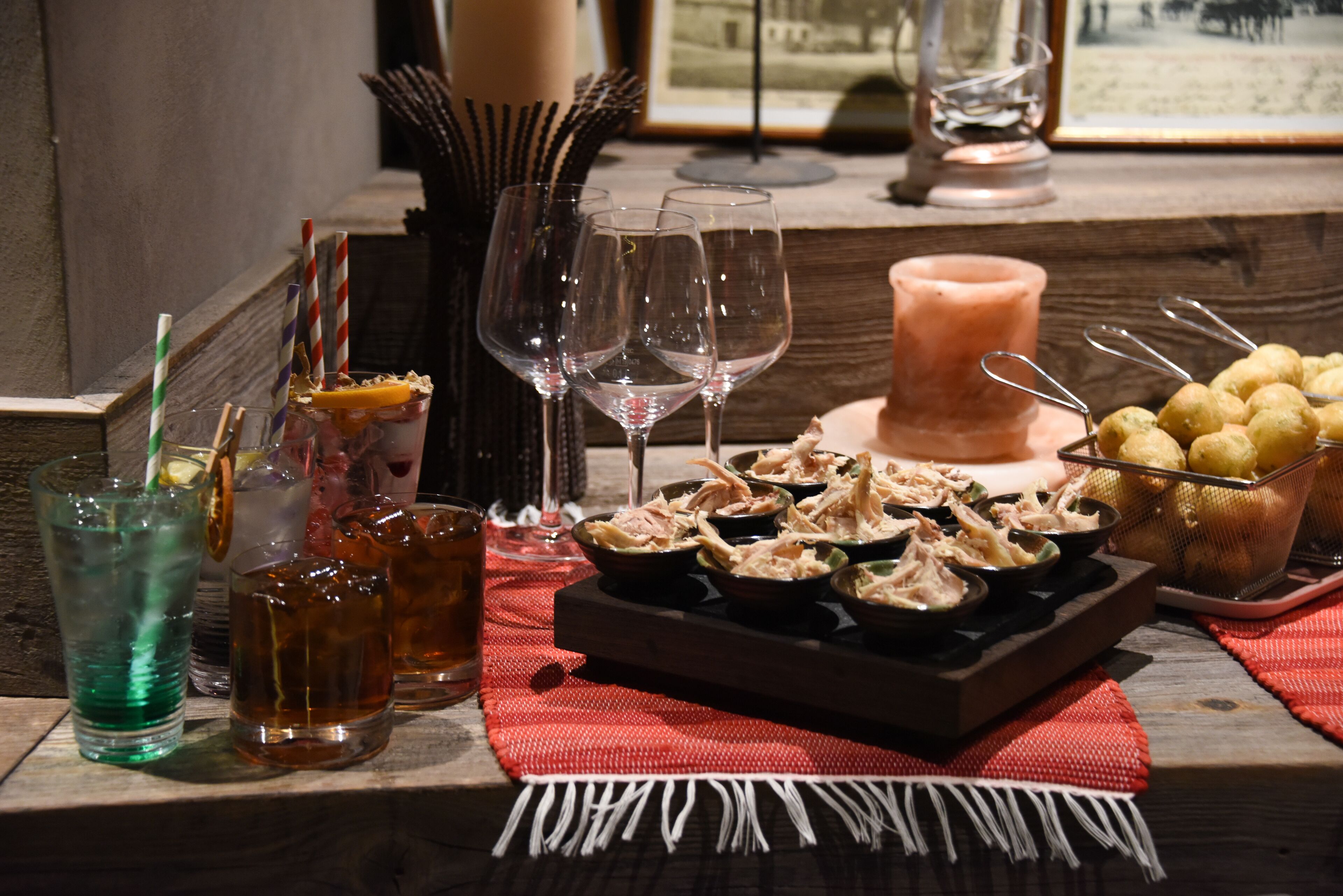 A table with various drinks, empty wine glasses, a candle, and a tray of food.