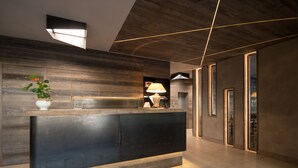 Una moderna zona de recepción con un mostrador oscuro, paneles de madera y un amplio ventanal que proporciona luz natural.