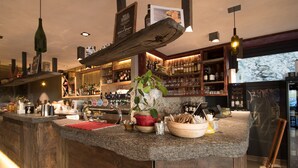 Una zona de bar con mostrador de madera, distintas botellas, copas y una planta en maceta.