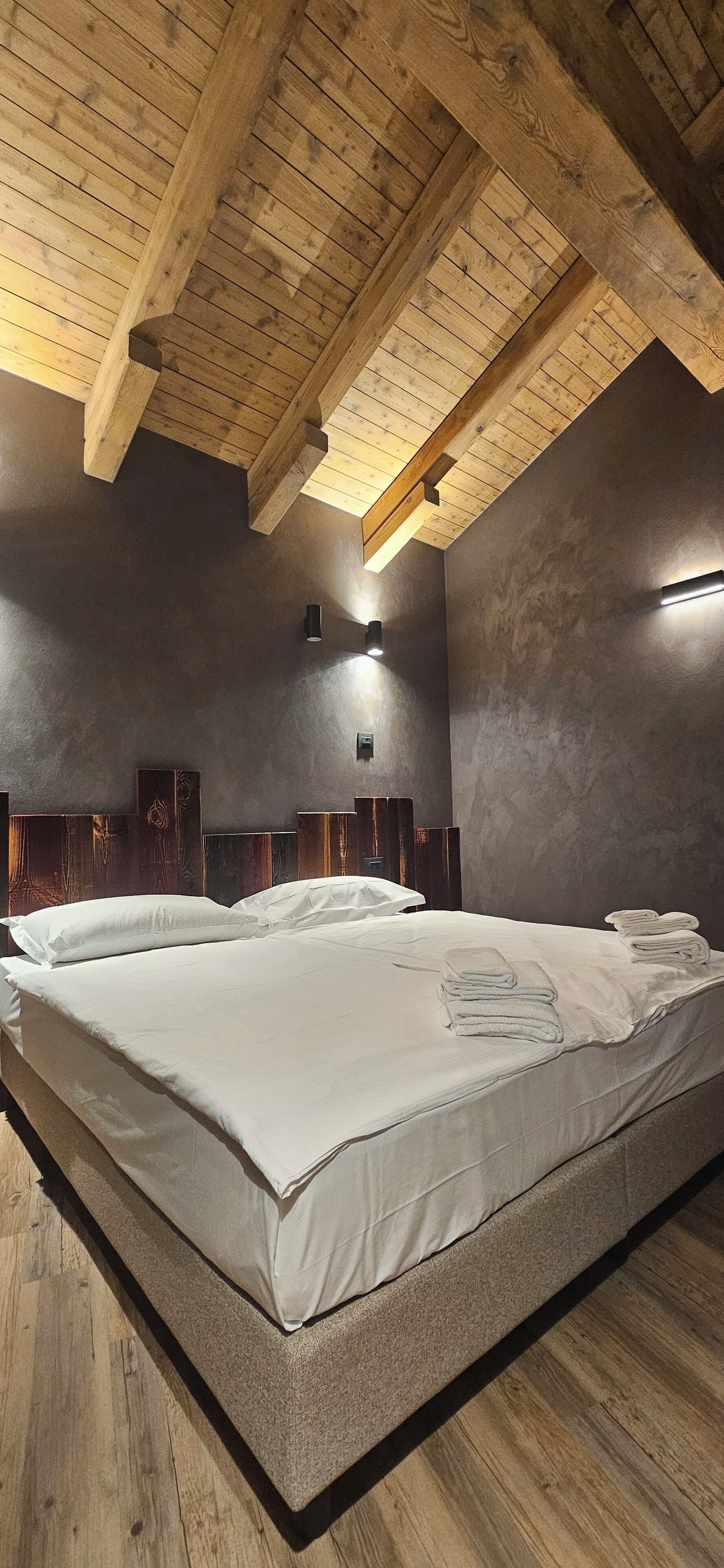 A bedroom with a large bed, wooden ceiling beams, and a textured wall.