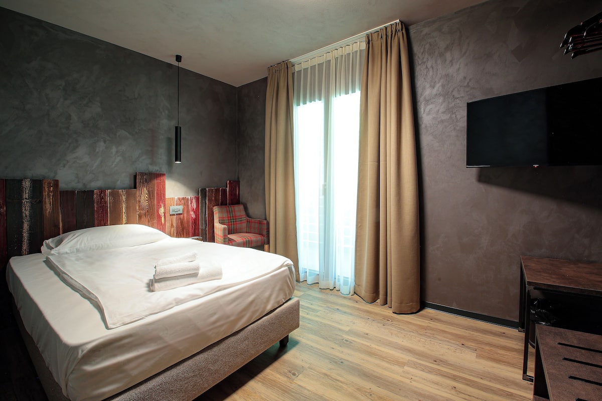 A hotel room with a large bed, a desk, a chair, a TV, and a window with curtains.