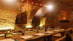 A restaurant with a rustic brick wall, wooden tables set with wine glasses and menus, and a mural on the wall.