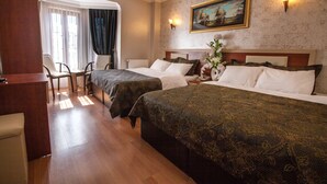 A hotel room with two beds, a desk, and a chair. There is a painting on the wall and a window with curtains.