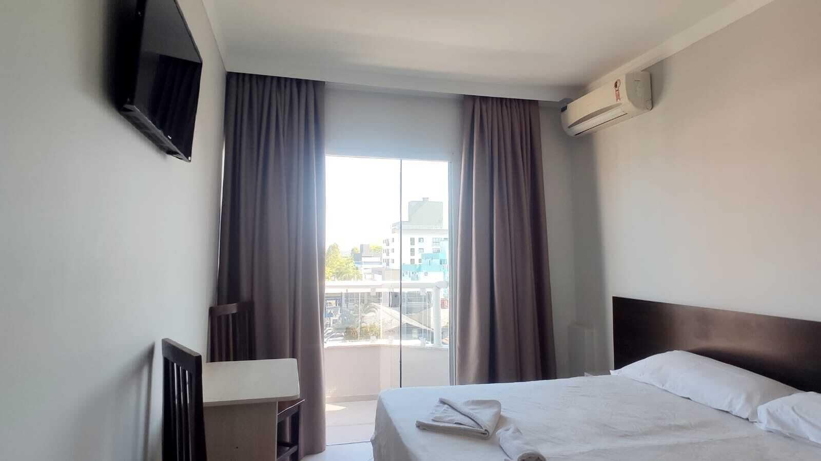 A hotel room with a bed, a desk, a TV, and a balcony with curtains.