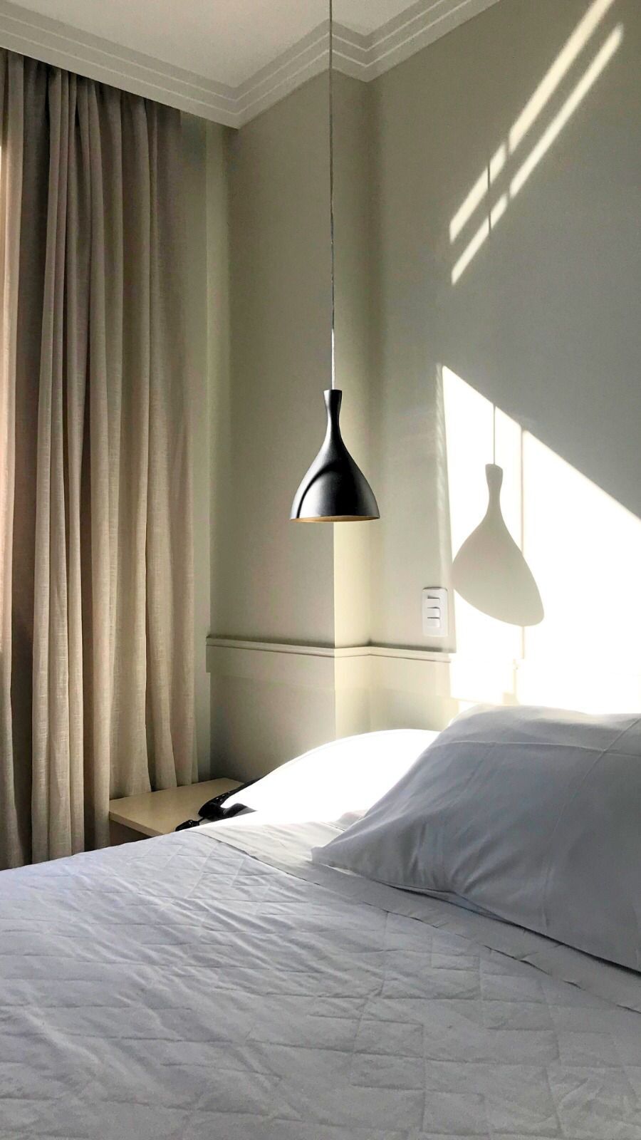 A hotel room with a bed, a nightstand, a lamp, and a window with curtains.