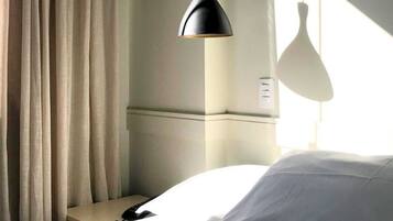 A hotel room with a bed, a nightstand, a lamp, and a window with curtains.