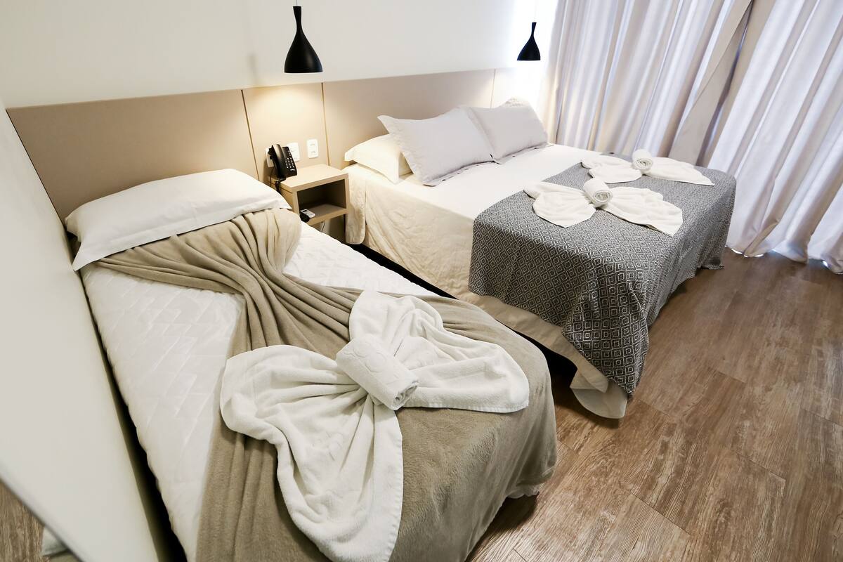 A hotel room with two beds, each with a different patterned bedspread, a bedside table with a lamp, and a wooden floor.