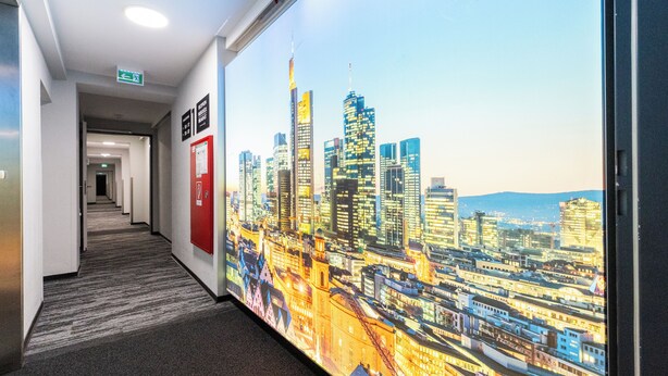 A hallway with a cityscape mural on the wall, a fire alarm, and a carpeted floor. - mk | hotel frankfurt (Frankfurt)