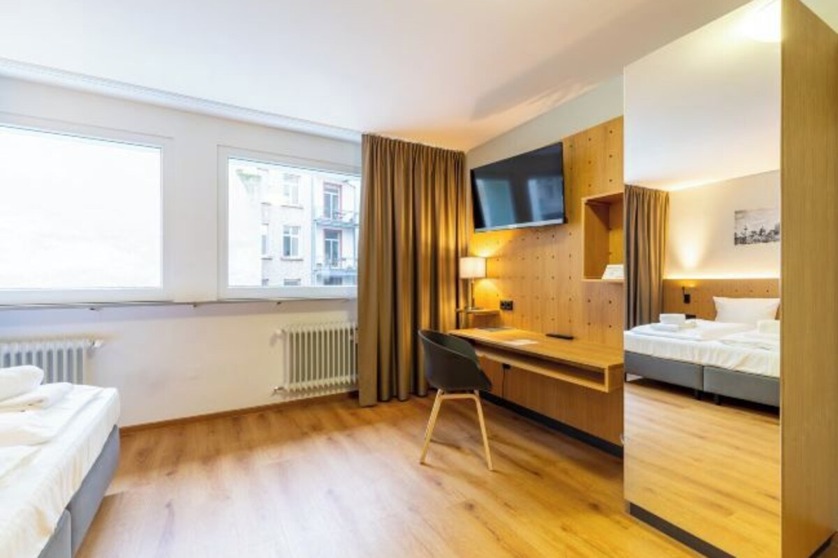 A hotel room with a bed, a desk, a chair, a TV, and a window with curtains.