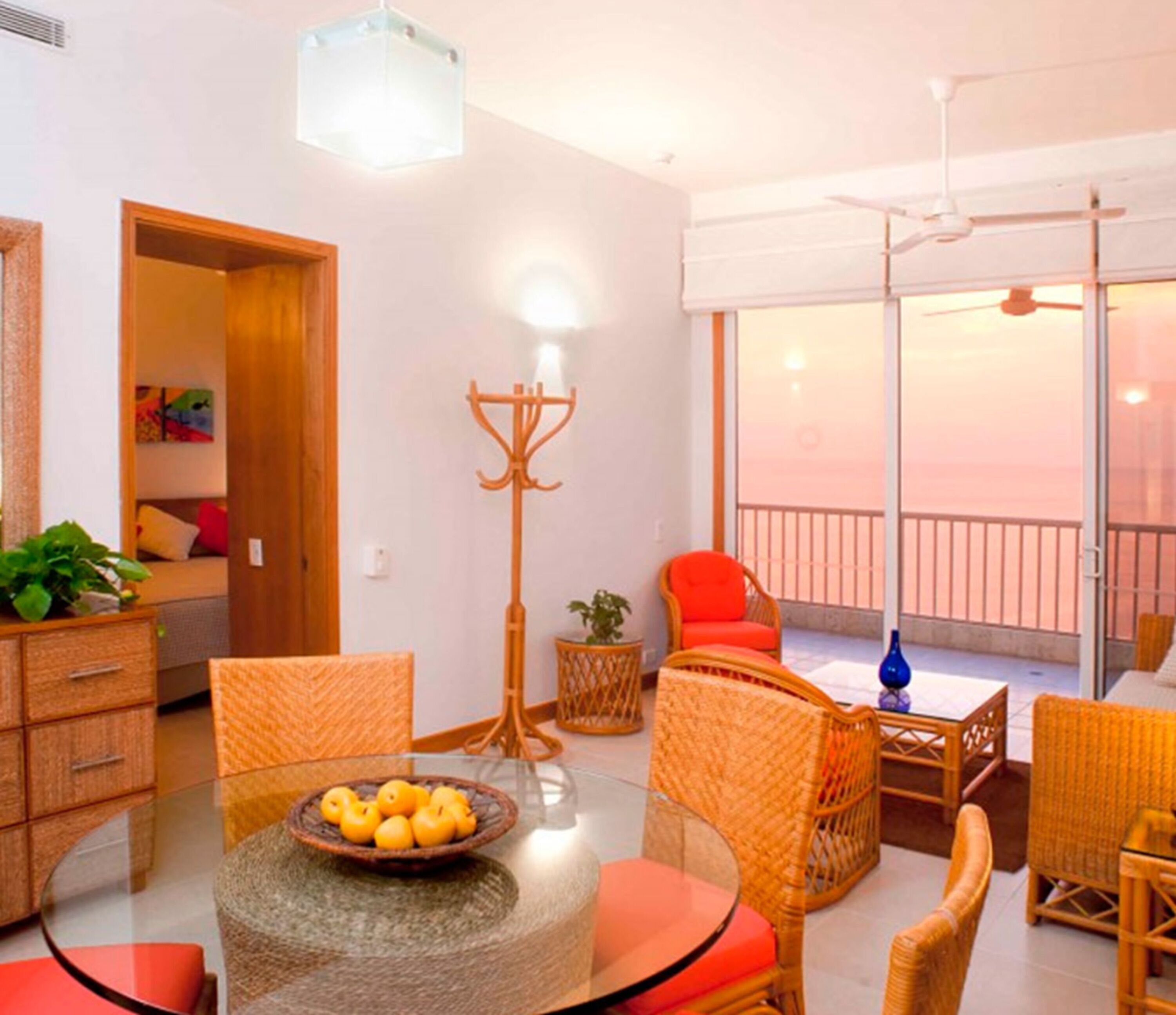 A modern living room with a glass table, wicker furniture, and a balcony with a view.