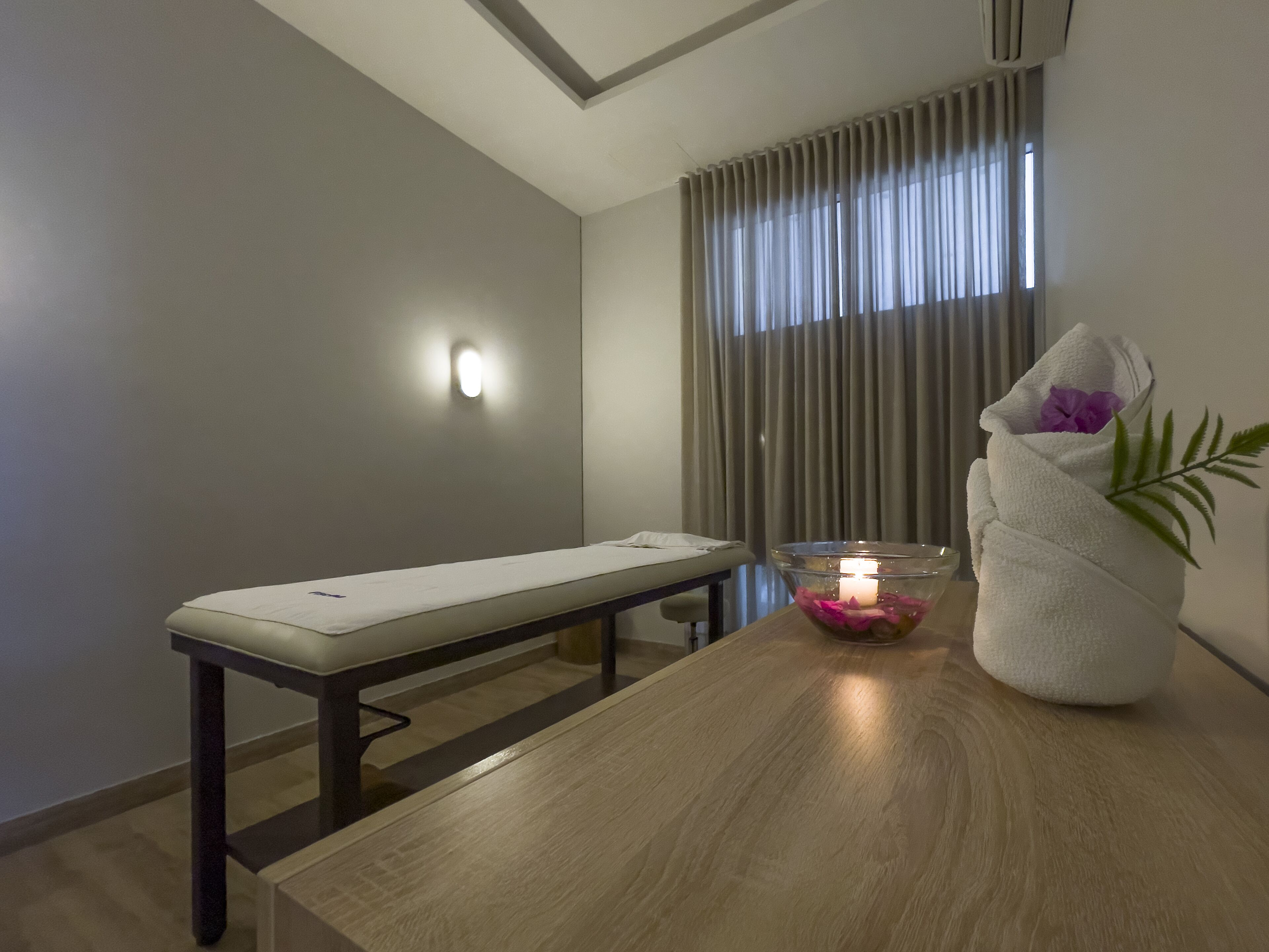 A modern room with a wooden table, a bench, a glass bowl with a candle, and a towel with a flower.