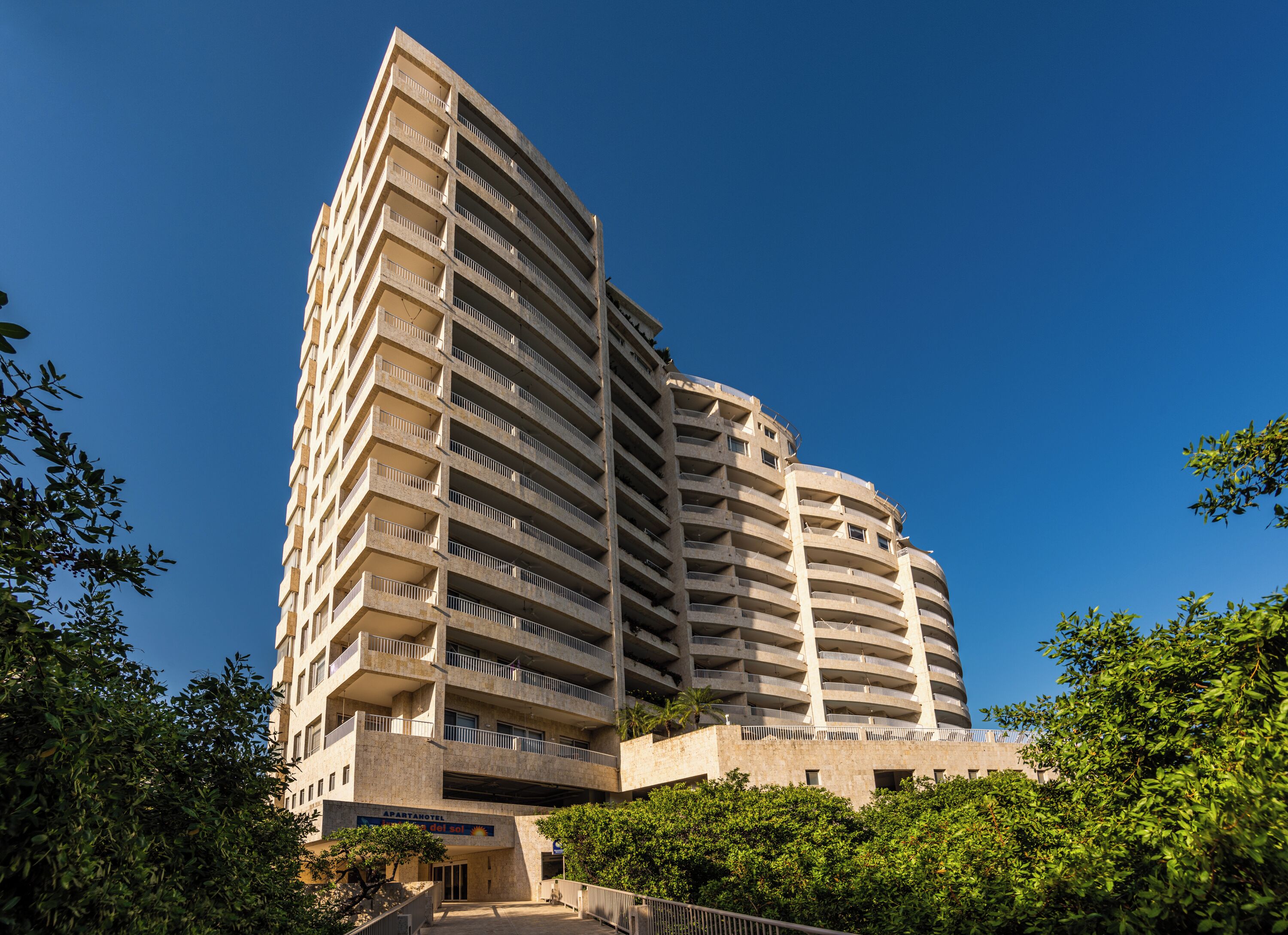 A multi-story hotel with balconies, a sun sign, and a sign indicating it is an apartment hotel.