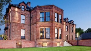 A large, multi-story brick building with a symmetrical facade, large windows, and a well-maintained lawn. - The Douglas Hotel (Isle of Arran)