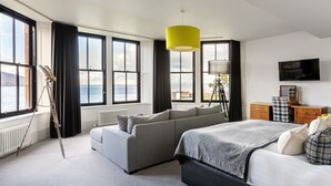 A modern hotel room with a large bed, a sofa, a desk, and a view of the sea. - The Douglas Hotel (Isle of Arran)