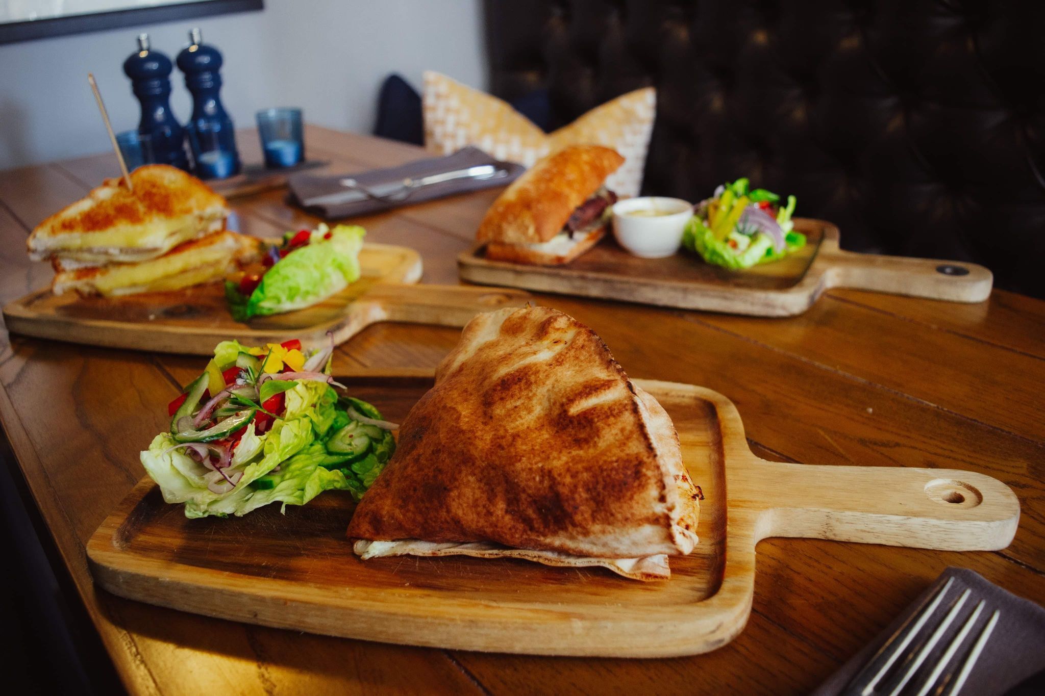 Een houten tafel met een belegd broodje en een salade op een houten plank.