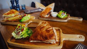 Een houten tafel met een belegd broodje en een salade op een houten plank.