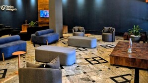 Un área de descanso moderna con sofás, otomanas y una mesa de centro, que presenta una pared oscura con un logotipo y un televisor.