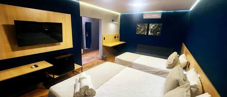 Habitación de hotel con dos camas, un escritorio, un televisor y un baño visible a través de una puerta abierta.