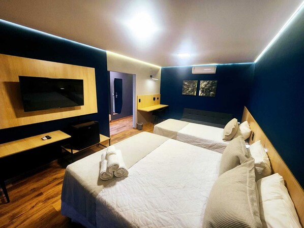 Habitación de hotel con dos camas, un escritorio, un televisor y un baño visible a través de una puerta abierta.