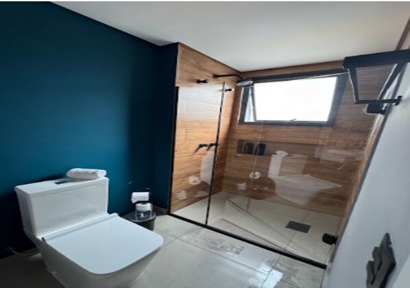 Een badkamer met een wit toilet, een douchecabine van glas en een raam.