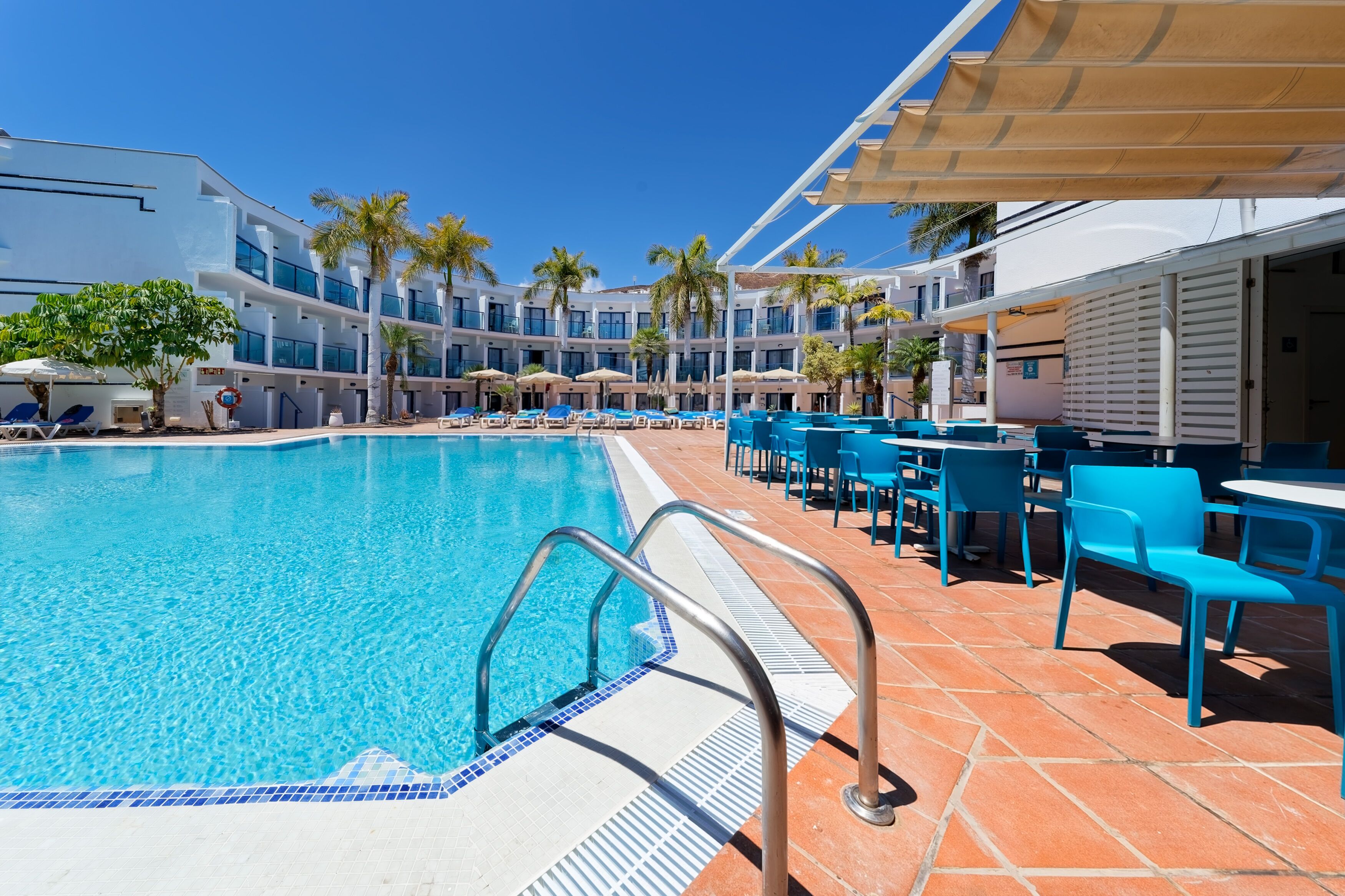 A hotel pool area with a clear blue pool, sun loungers, and umbrellas.