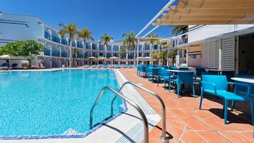 A pool area with a clear blue pool, sun loungers, and umbrellas.