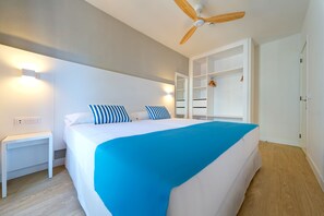 Une chambre à coucher comprenant un lit, une table de chevet, un ventilateur de plafond, une armoire et un miroir.