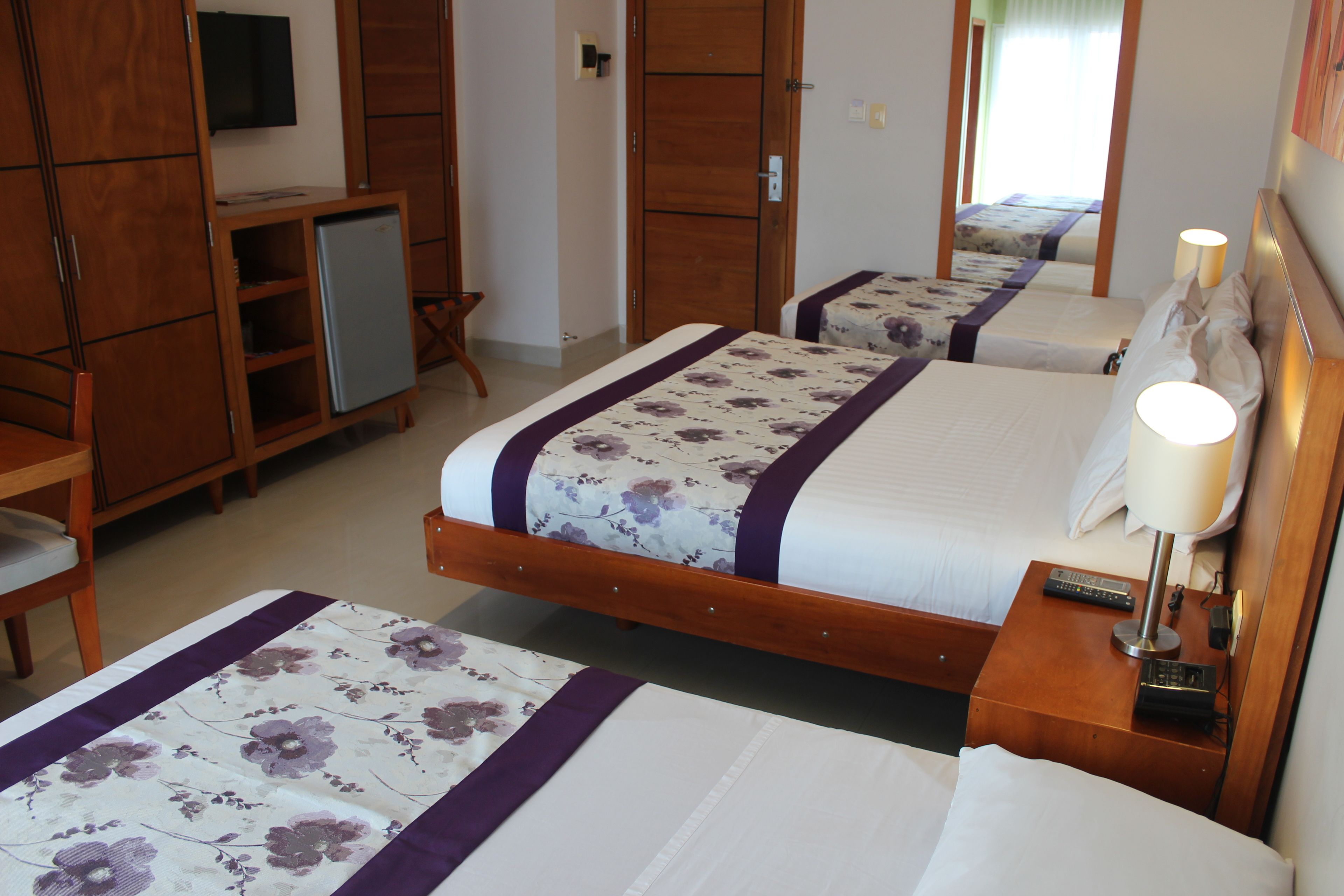 Une chambre d’hôtel avec deux lits, une télévision, un petit réfrigérateur et une armoire en bois.