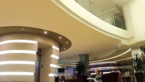 Un vestíbulo espacioso con techo curvo, una mesa de recepción, zonas de estar y una escalera que conduce a un nivel superior.