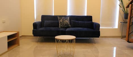 Una sala de estar moderna con un sofá azul oscuro, una mesa de centro redonda de madera y una planta en maceta.